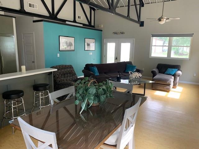 dining space featuring ceiling fan, french doors, a towering ceiling, and light wood-type flooring