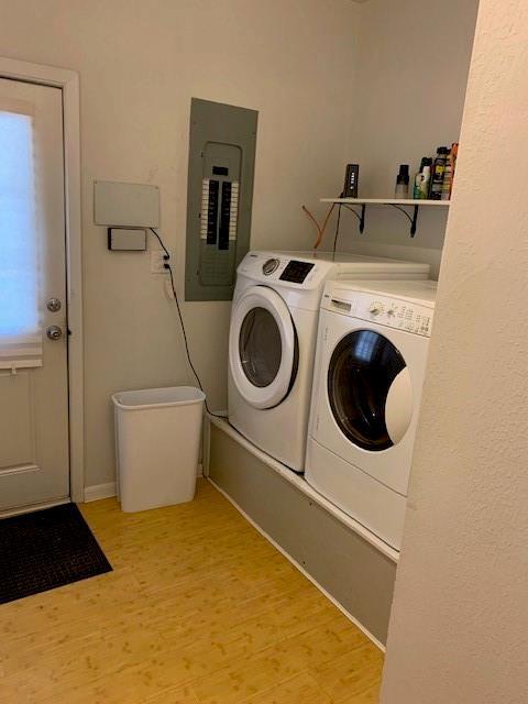 laundry area with light wood-type flooring, electric panel, and washing machine and clothes dryer