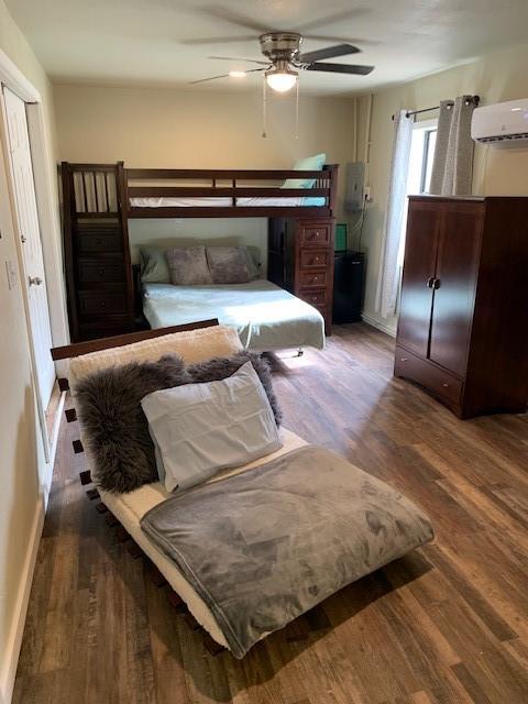 bedroom with ceiling fan, dark hardwood / wood-style flooring, and a wall unit AC