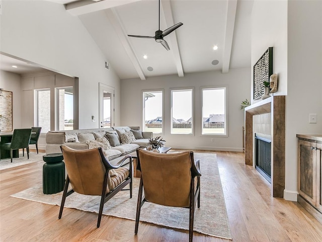 living room with high vaulted ceiling, light hardwood / wood-style flooring, ceiling fan, beam ceiling, and a tiled fireplace