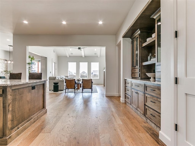 kitchen with ceiling fan, hanging light fixtures, light stone counters, lofted ceiling with beams, and light hardwood / wood-style floors