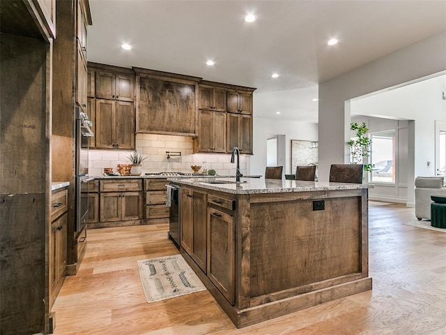 kitchen with light stone countertops, sink, beverage cooler, a kitchen island with sink, and light wood-type flooring