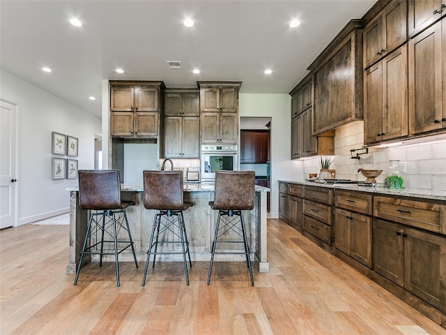 kitchen with a kitchen bar, light stone countertops, stainless steel appliances, a kitchen island with sink, and light hardwood / wood-style floors