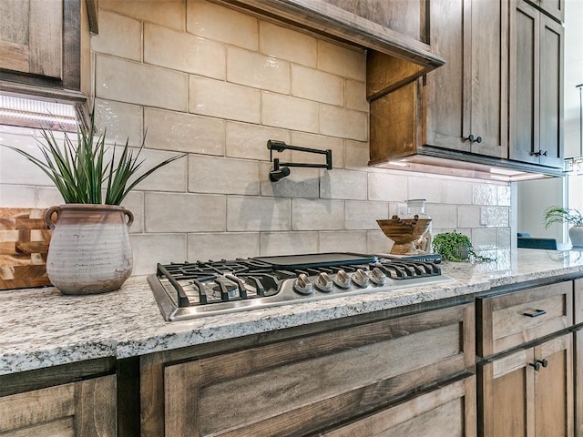 interior details featuring light stone countertops, backsplash, and stainless steel gas cooktop