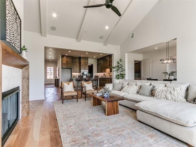 living room featuring ceiling fan, a tile fireplace, high vaulted ceiling, beamed ceiling, and light hardwood / wood-style floors