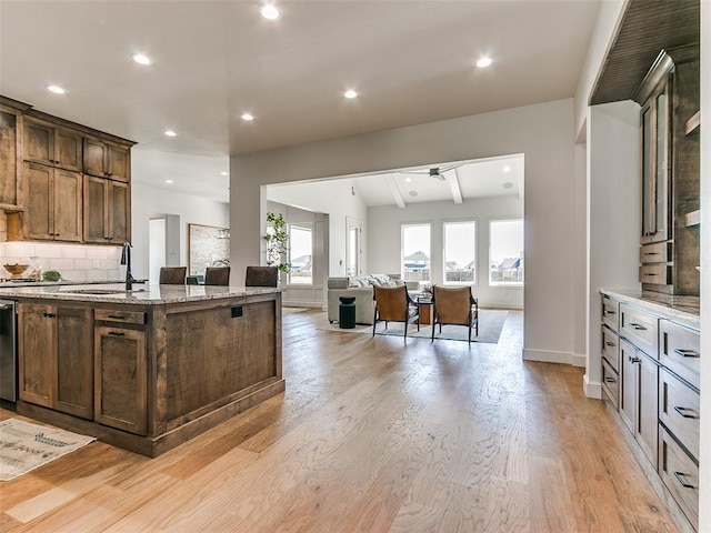 kitchen with a center island with sink, light hardwood / wood-style flooring, sink, backsplash, and light stone countertops