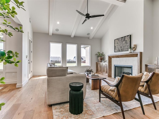 living room with a tile fireplace, light wood-type flooring, ceiling fan, and lofted ceiling with beams