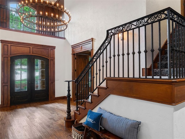 foyer entrance featuring wood-type flooring, an inviting chandelier, french doors, and a high ceiling