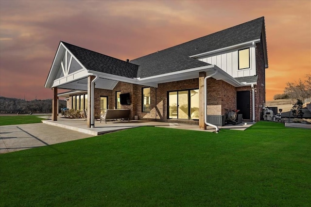 back house at dusk featuring a lawn and a patio area