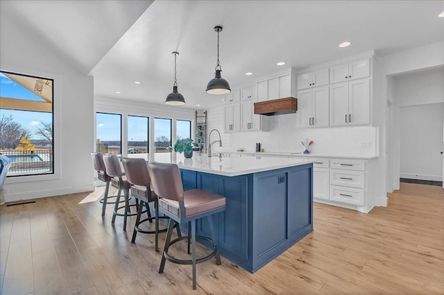 kitchen with light wood-type flooring, an island with sink, a breakfast bar, white cabinetry, and decorative light fixtures