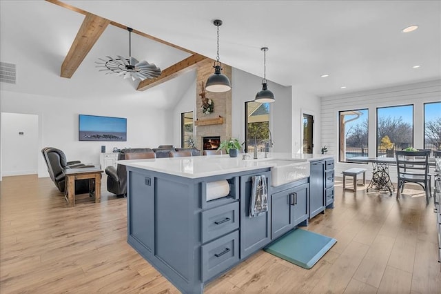 kitchen with an island with sink, ceiling fan, pendant lighting, a fireplace, and light hardwood / wood-style flooring