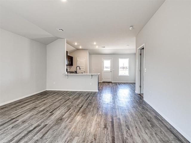 unfurnished living room featuring sink, dark wood-type flooring, and vaulted ceiling