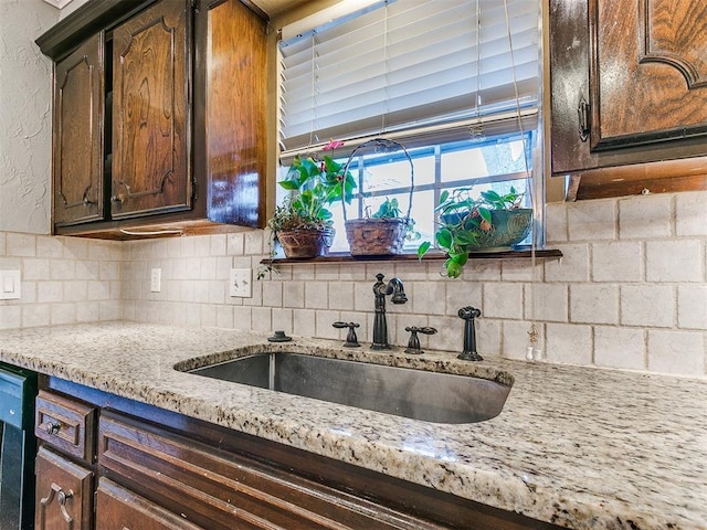 kitchen with backsplash, dark brown cabinets, light stone counters, and sink