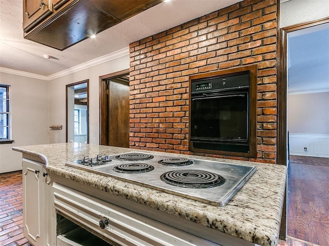 kitchen featuring black oven, stainless steel stovetop, ornamental molding, and light stone counters