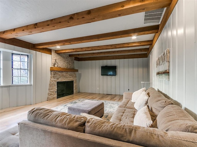 living room with beamed ceiling, light hardwood / wood-style floors, and a stone fireplace