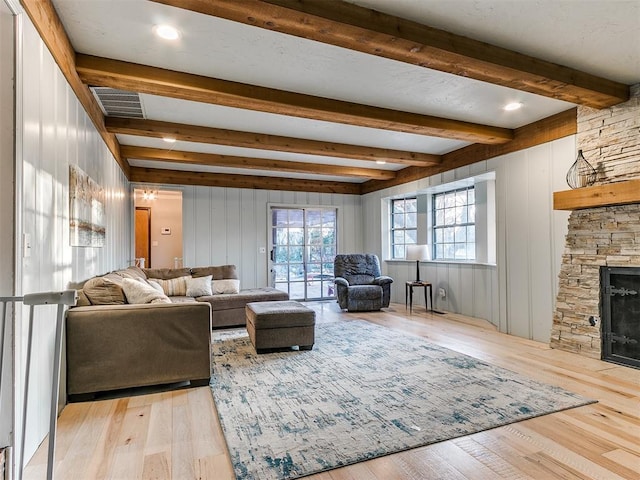 living room featuring a stone fireplace, wood walls, beamed ceiling, and light wood-type flooring