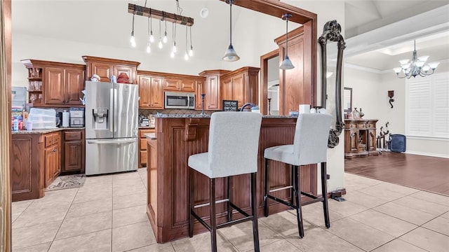 kitchen featuring a kitchen bar, appliances with stainless steel finishes, light stone countertops, pendant lighting, and a notable chandelier