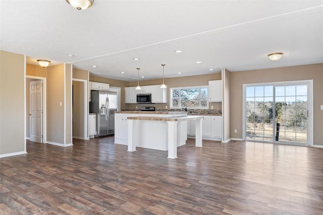 kitchen with appliances with stainless steel finishes, a breakfast bar, decorative light fixtures, white cabinets, and a center island