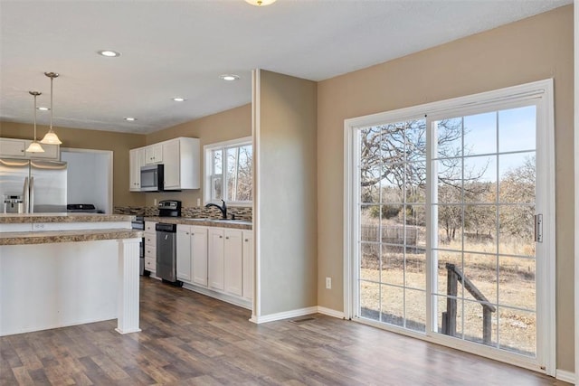 kitchen featuring white cabinetry, sink, dark wood-type flooring, hanging light fixtures, and stainless steel appliances