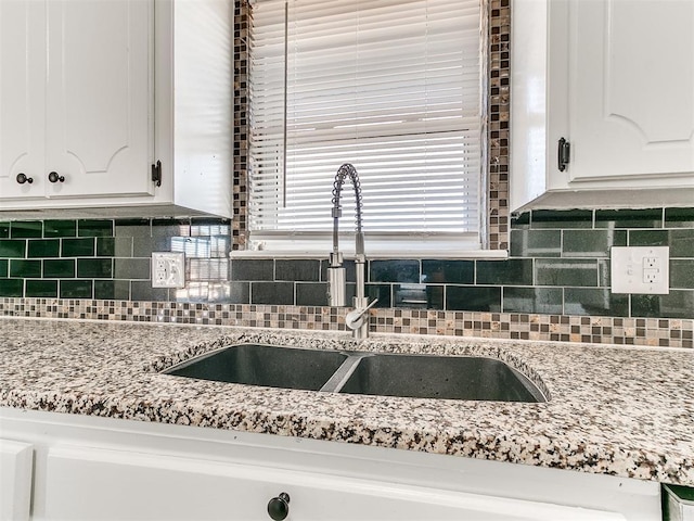 room details featuring white cabinets, backsplash, light stone counters, and sink