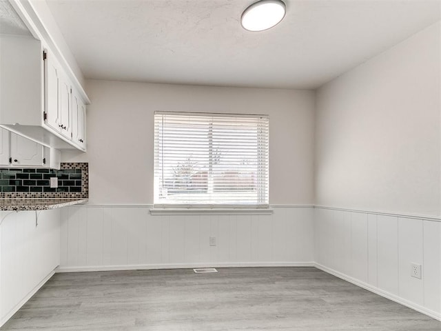 interior space featuring light wood-type flooring, white cabinetry, and tasteful backsplash