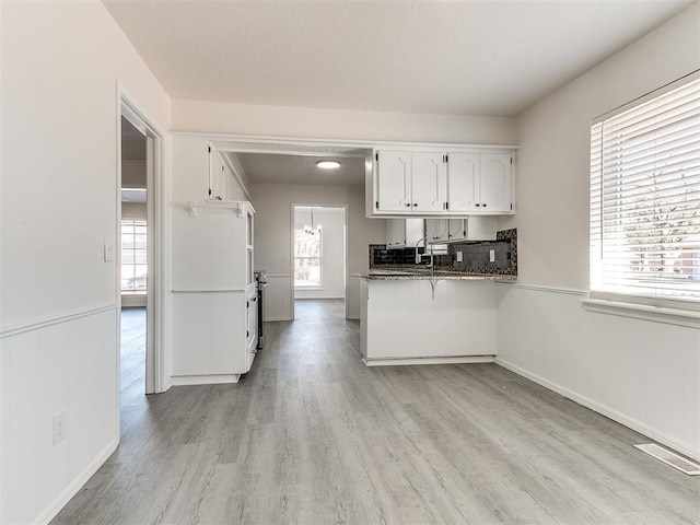 kitchen featuring white cabinetry, kitchen peninsula, dark stone counters, and light hardwood / wood-style flooring