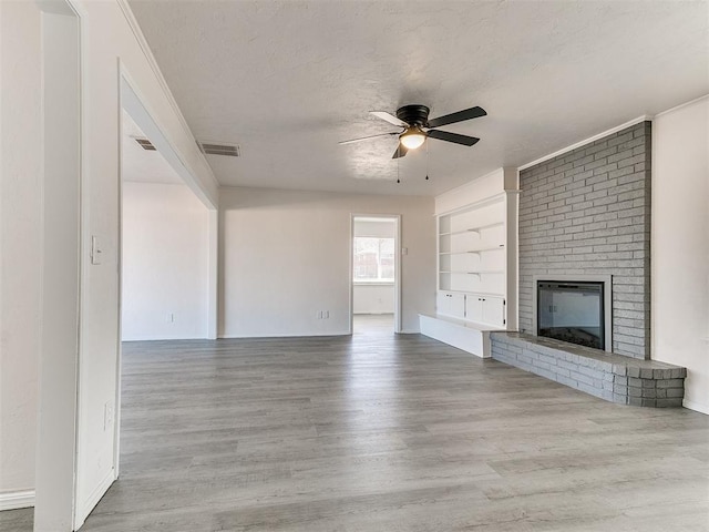 unfurnished living room featuring built in shelves, a textured ceiling, ceiling fan, light hardwood / wood-style flooring, and a fireplace