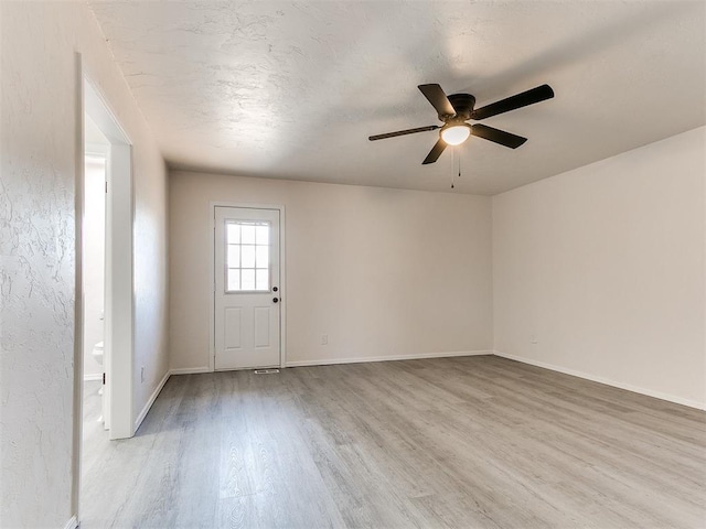 unfurnished room with ceiling fan, a textured ceiling, and light wood-type flooring