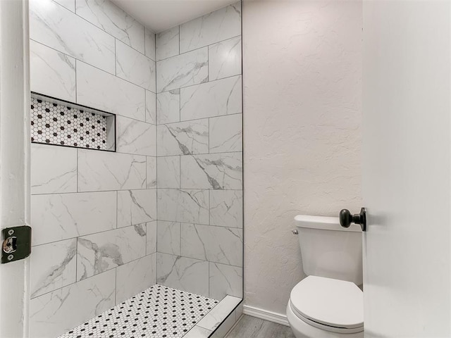 bathroom with toilet, wood-type flooring, and tiled shower