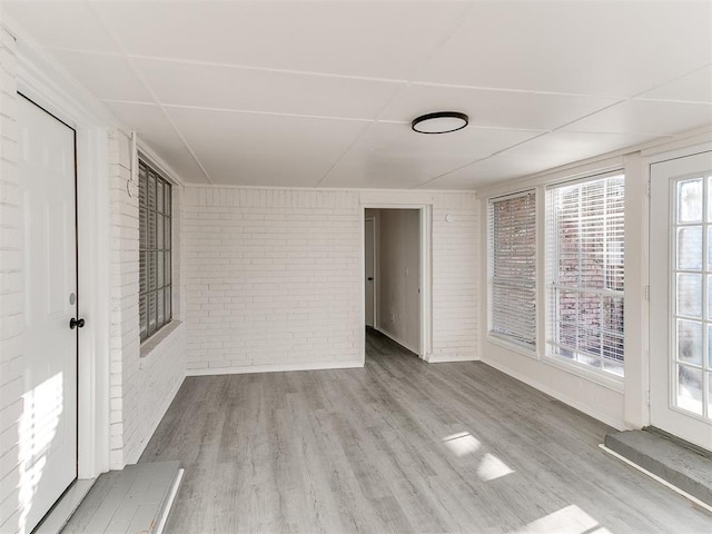 unfurnished room with brick wall and light wood-type flooring