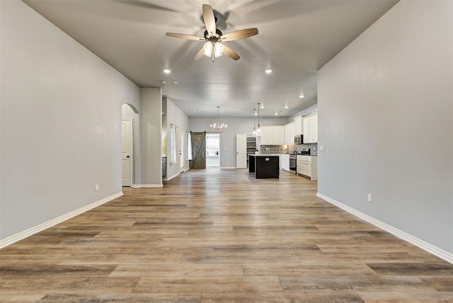 unfurnished living room featuring ceiling fan with notable chandelier and light hardwood / wood-style flooring