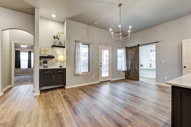 kitchen with hanging light fixtures, a barn door, ceiling fan with notable chandelier, and light wood-type flooring