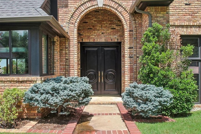 entrance to property with brick siding and a shingled roof