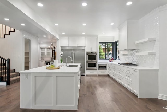 kitchen featuring decorative backsplash, a center island with sink, white cabinets, custom range hood, and appliances with stainless steel finishes