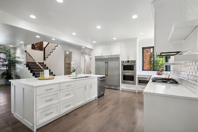 kitchen featuring dark wood-type flooring, a center island with sink, sink, appliances with stainless steel finishes, and white cabinetry