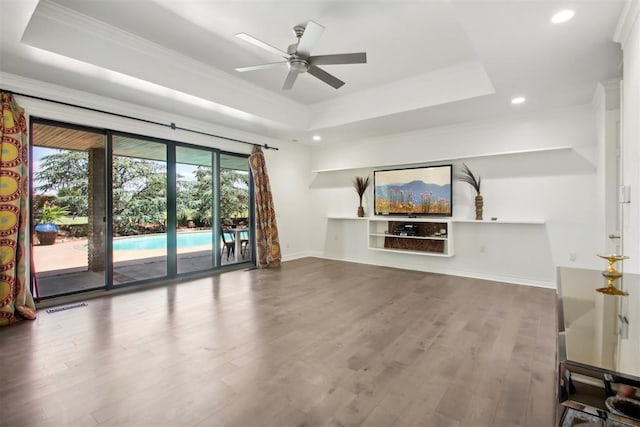 unfurnished living room with a raised ceiling, recessed lighting, wood finished floors, and ornamental molding