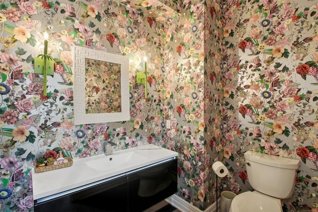 half bathroom with toilet, vanity, and wallpapered walls