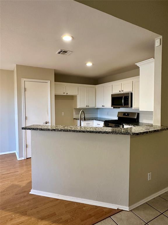 kitchen featuring white cabinets, kitchen peninsula, stainless steel appliances, and dark stone counters