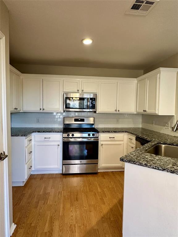 kitchen featuring appliances with stainless steel finishes, sink, dark stone countertops, light hardwood / wood-style floors, and white cabinetry