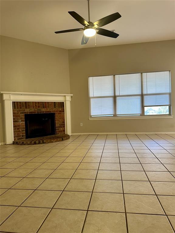 unfurnished living room featuring ceiling fan, light tile patterned floors, and a brick fireplace