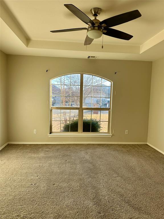 carpeted empty room with a raised ceiling and ceiling fan