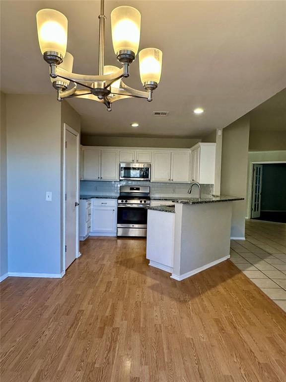 kitchen with white cabinets, hanging light fixtures, tasteful backsplash, a notable chandelier, and stainless steel appliances