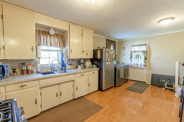 kitchen with backsplash, sink, light wood-type flooring, stainless steel refrigerator, and washing machine and clothes dryer