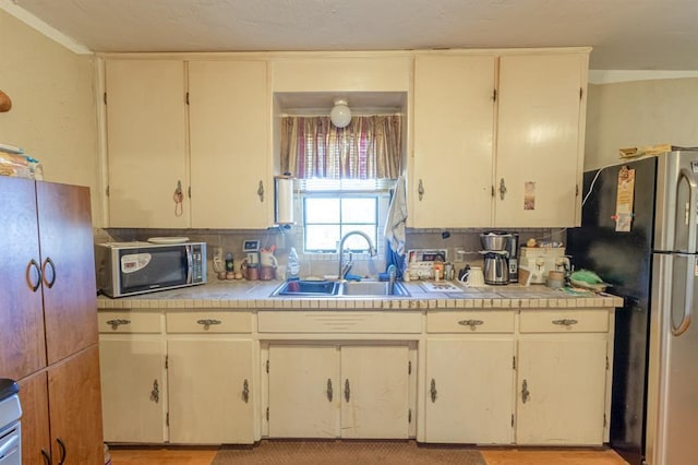 kitchen with backsplash, stainless steel fridge, sink, and tile counters