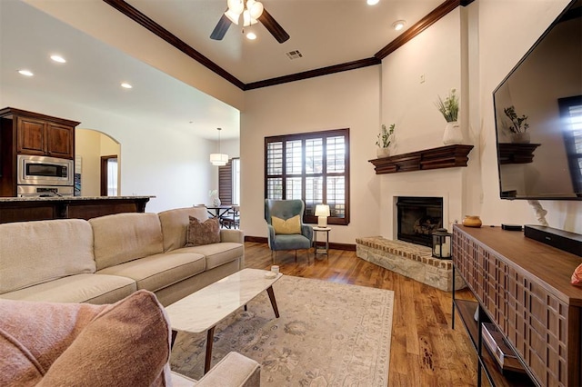 living room with a fireplace, light wood-type flooring, ceiling fan, and crown molding