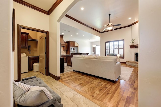 living room featuring ceiling fan, washer / dryer, ornamental molding, and light hardwood / wood-style flooring