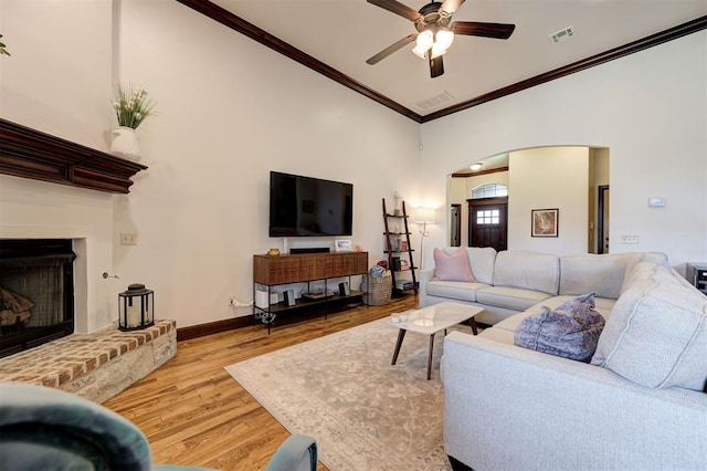 living room with high vaulted ceiling, crown molding, a brick fireplace, ceiling fan, and light hardwood / wood-style floors