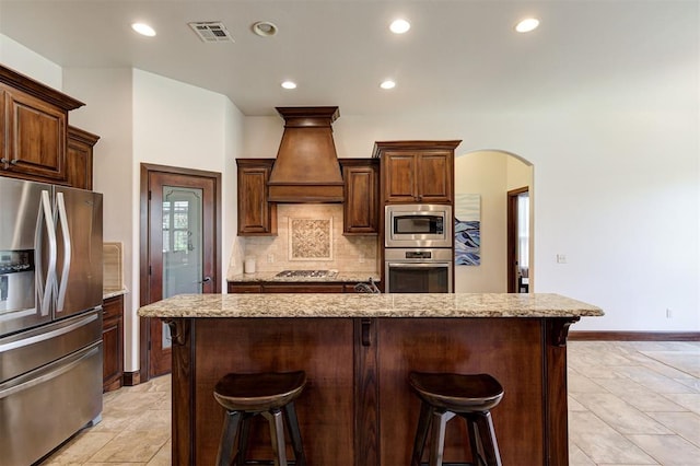 kitchen featuring a center island with sink, custom exhaust hood, a kitchen bar, and stainless steel appliances