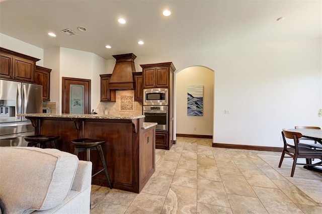 kitchen with a center island with sink, backsplash, premium range hood, and stainless steel appliances