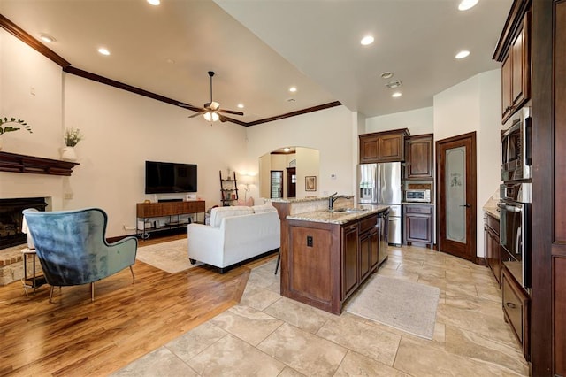 kitchen featuring stainless steel appliances, ceiling fan, crown molding, sink, and a center island with sink